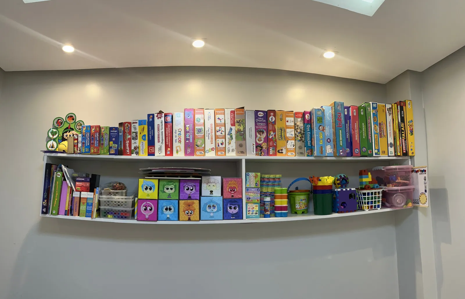 Prateleiras com jogos de tabuleiro, livros infantis, caixas coloridas e brinquedos de encaixe