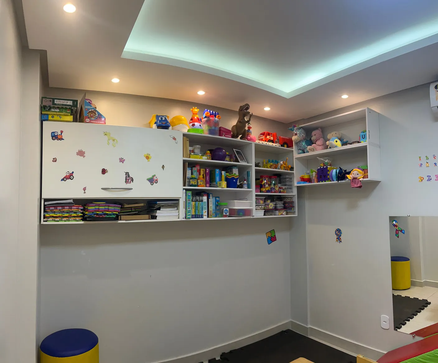 Sala de fonoaudiologia, com armários de jogos, livros e brinquedos ao alcance da terapeuta.