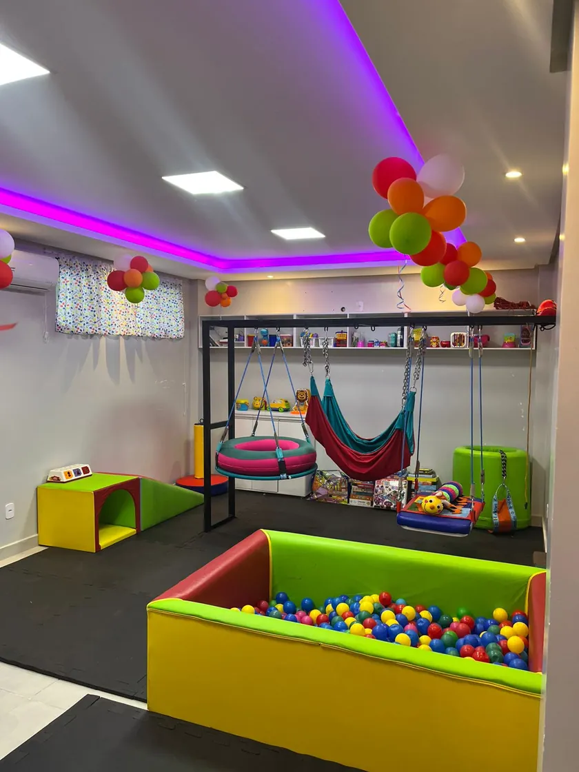 Sala de integração sensorial, com piscina de bolinhas, rede, balanços e luz colorida no teto.